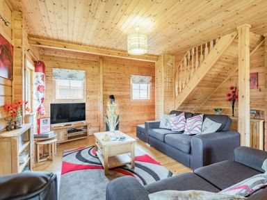 A living room with gray sofas a wooden coffee table a TV and wooden staircase at Robin Lodge in Llanbedr