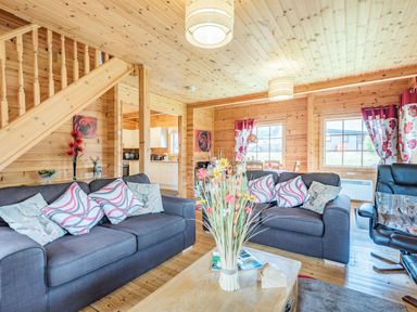 A living room with two gray sofas and a black armchair with cushions and flowers on a wooden table at Robin Lodge in Llanbedr