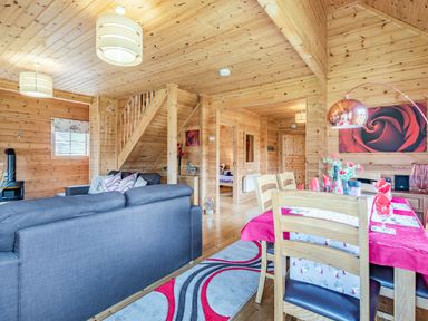 A wooden interior living and dining area with grey sofas a dining table with red napkins and a rose painting on the wall at Robin Lodge in Llanbedr
