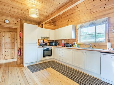 A wooden kitchen with white cabinets oven microwave and window blinds at Robin Lodge in Llanbedr