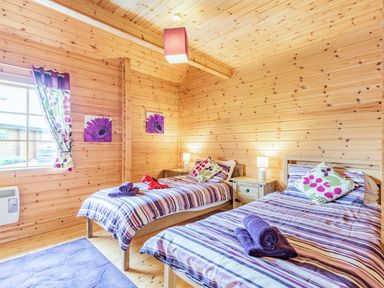 A bedroom with two single beds wooden walls a window and bedside tables at Robin Lodge in Llanbedr
