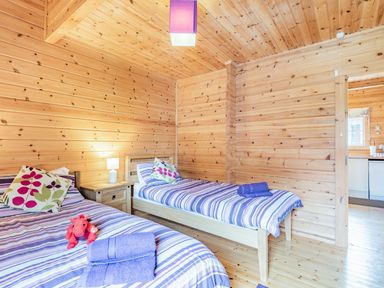 A bedroom with two single beds striped bedding and wooden walls at Robin Lodge in Llanbedr