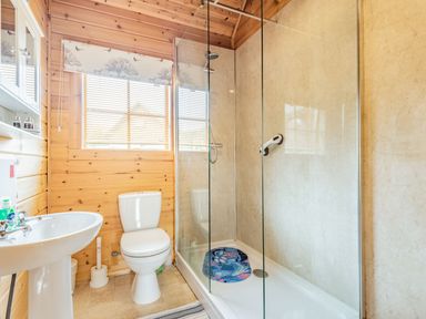 A bathroom with a toilet sink and shower with glass panel at Robin Lodge in Llanbedr