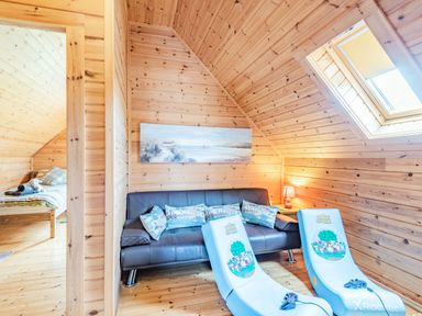 A wooden room with a black sofa and two gaming chairs with controllers and a window at Robin Lodge in Llanbedr