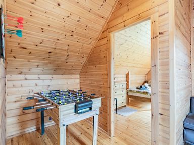 A foosball table and darts on a wall in a wooden game room with a bedroom visible through a doorway at Robin Lodge in Llanbedr