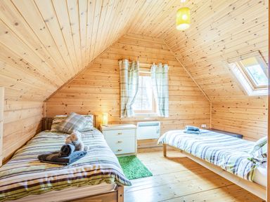A bedroom with two single beds a window with curtains a small dresser and wooden walls and ceiling at Robin Lodge in Llanbedr