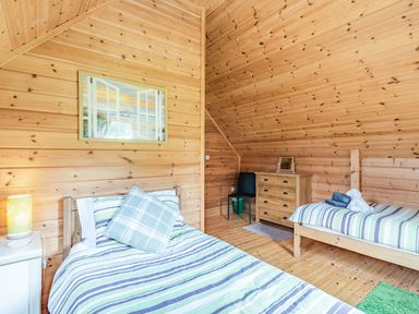 A bedroom with two single beds a wooden dresser a black chair and wooden paneled walls at Robin Lodge in Llanbedr