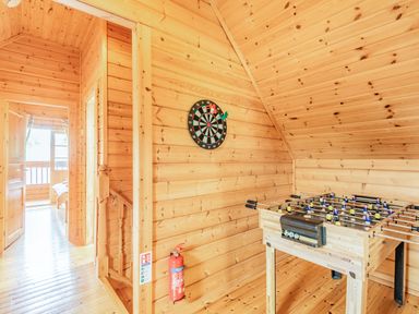 A wooden room with a foosball table dartboard fire extinguisher and open door leading to another room at Robin Lodge in Llanbedr