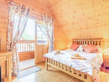A bedroom with a wooden bed and floral bedding next to a door with floral curtains at Robin Lodge in Llanbedr