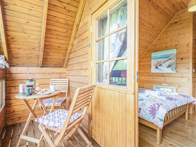 A wooden interior with a small table and two chairs with cushions and a bed with floral bedding at Robin Lodge in Llanbedr