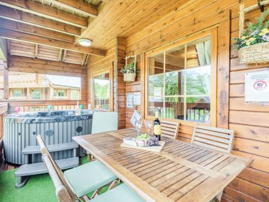 A wooden outdoor patio with a hot tub and a wooden dining table with chairs at Robin Lodge in Llanbedr