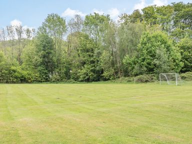 A grass field with a soccer goal and trees in the background at Robin Lodge in Llanbedr