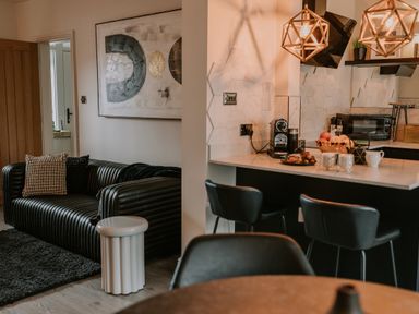 A living area with a black ribbed sofa and cushions next to a kitchen with bar stools and a countertop at 37 Jubilee Street in Llandudno