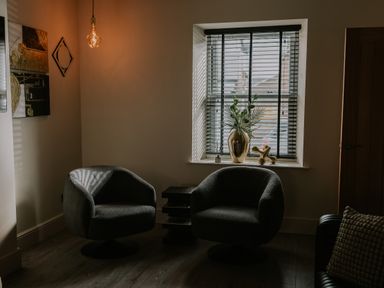 A room with two armchairs a small table window with blinds and decorative items on the windowsill at 37 Jubilee Street in Llandudno