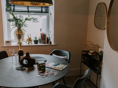 A dining area with a round table, black chairs, a window with a vase, books, and decorative items at 37 Jubilee Street in Llandudno
