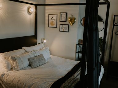 A bedroom with a four-poster bed white bedding wall art and a small shelving unit at 37 Jubilee Street in Llandudno