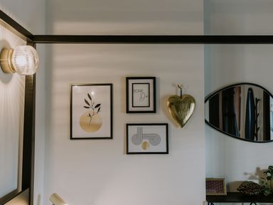 A wall with three framed pictures a gold heart decoration a wall lamp and an oval mirror at 37 Jubilee Street in Llandudno