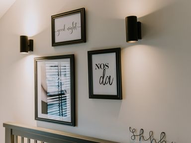 Three framed pictures with black frames on a wall above a bed headboard with two black wall lamps at 37 Jubilee Street in Llandudno