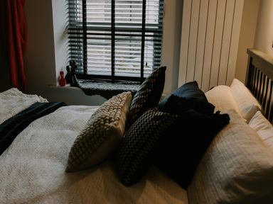 A bedroom with a bed with pillows near a window with blinds and two small decorative figures at 37 Jubilee Street in Llandudno