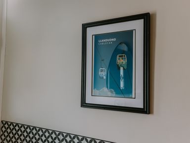 A framed poster of Llandudno cablecar on a plain light-colored wall above a patterned tile backsplash at 37 Jubilee Street in Llandudno