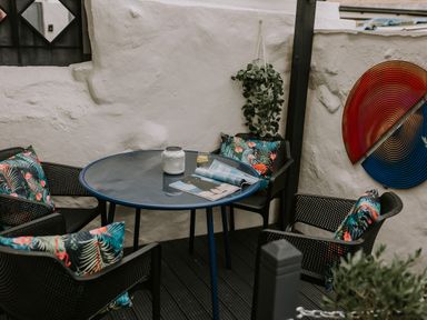 An outdoor seating area with a round glass table and four chairs with tropical print cushions at 37 Jubilee Street Llandudno