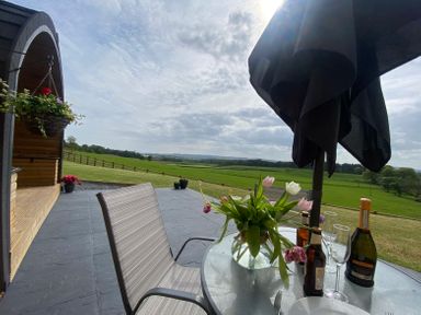 A patio with a table and chairs overlooking a green field at Cleugh Lodge in Lockerbie