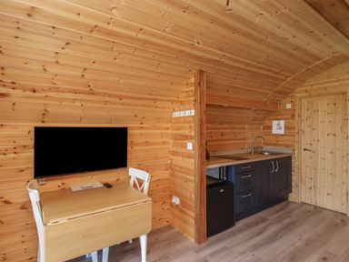 A small wooden kitchen area with a table and chairs and a wall mounted TV at Cleugh Lodge in Lockerbie