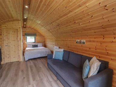 An interior room with wooden walls a bed and a sofa with cushions at Cleugh Lodge in Lockerbie
