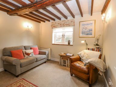 A living room with a gray sofa and brown leather armchair with wooden ceiling beams at Cosy Cottage in Bawdeswell