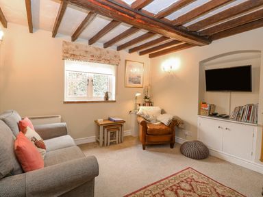 A sitting room with a grey sofa and brown armchair under wooden beam ceiling at Cosy Cottage in Bawdeswell