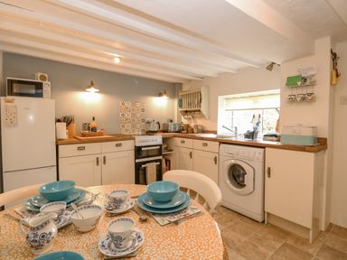 A kitchen with a round table set with blue and white dishes a refrigerator oven washing machine and window at Cosy Cottage in Bawdeswell