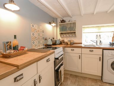 A kitchen with white cabinets wooden countertops an electric stove a kettle a toaster and a washing machine at Cosy Cottage in Bawdeswell
