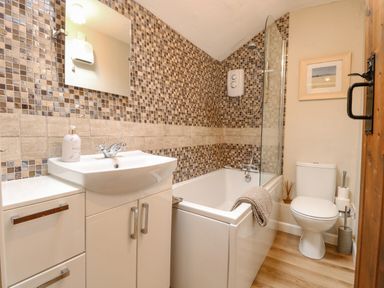 A bathroom with a bathtub shower sink toilet and mosaic tiled walls at Cosy Cottage in Bawdeswell