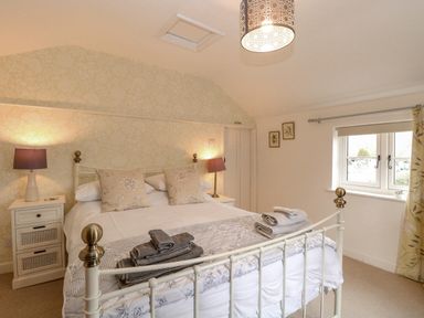 A bedroom with a metal bed frame bedside tables with lamps folded towels on the bed and a window at Cosy Cottage in Bawdeswell