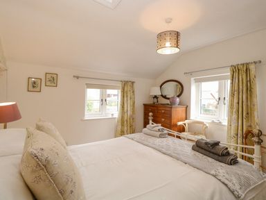 A bedroom with a bed pillows folded towels wooden dresser mirror curtains and two windows at Cosy Cottage in Bawdeswell