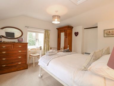 A bedroom with a bed a wooden chest of drawers a chair and a wooden wardrobe at Cosy Cottage in Bawdeswell