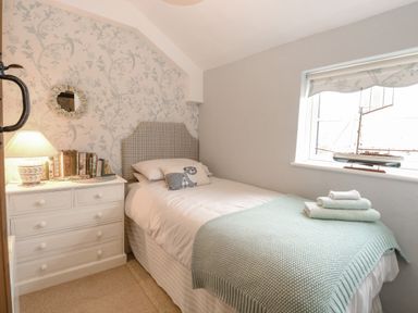 A small bedroom with a single bed beside a chest of drawers and a model ship on the windowsill at Cosy Cottage in Bawdeswell