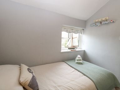 A bedroom with a single bed a pillow folded towels a blanket and a model sailboat on the windowsill at Cosy Cottage in Bawdeswell