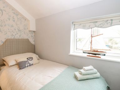 A bedroom with a bed with a checkered headboard and a model sailboat on the window at Cosy Cottage in Bawdeswell