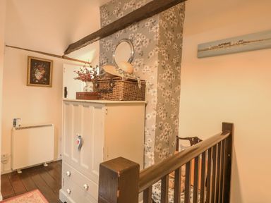 A hallway with a white cabinet, a wicker basket with a hat on top, floral wallpaper, and a wooden railing at Cosy Cottage in Bawdeswell