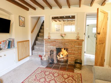 A living room with a fireplace a staircase and an open door at Cosy Cottage in Bawdeswell