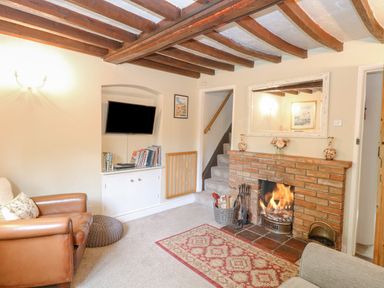 A living room with a brick fireplace a television on a built-in shelf and wooden ceiling beams at Cosy Cottage in Bawdeswell