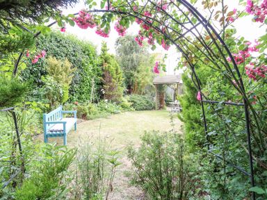 A garden with a blue bench and a metal arch with pink flowers at Cosy Cottage in Bawdeswell