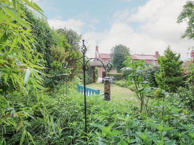 A garden with bird feeders plants a blue bench and a table and chairs at Cosy Cottage in Bawdeswell
