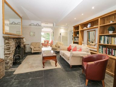 A living room with a stone fireplace armchairs a striped sofa wooden coffee table and wooden bookshelves at Valley View in Dalton-In-Furness