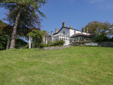 A house with a glass conservatory and stone walls on a grass slope with trees at Valley View in Dalton-In-Furness