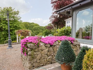 A stone planter with pink flowers outside a house with a window and potted plants at Valley View in Dalton-In-Furness