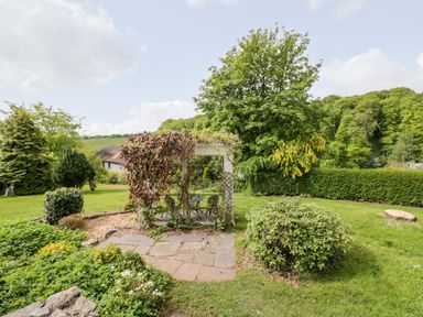 A garden with a small pergola covered in vines surrounded by shrubs and trees at Valley View in Dalton-In-Furness