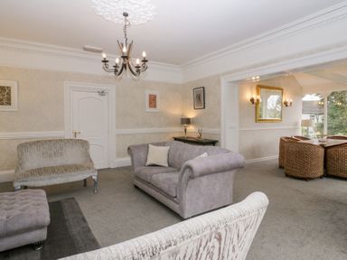 A living room with grey sofas and chandelier next to a dining area with wicker chairs at Valley View in Dalton-In-Furness