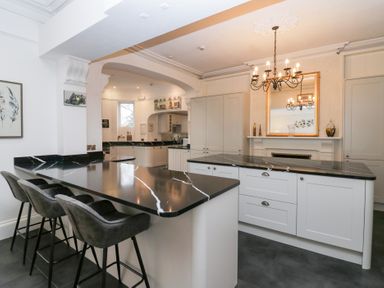 A kitchen with black marble countertops grey bar stools and a chandelier above a fireplace at Valley View in Dalton-In-Furness